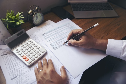 Sensible Services ABC in Hammond La - Accounting Services image of married businessman's hands filling out business tax forms at desk with small calculator, clock and plant on desk