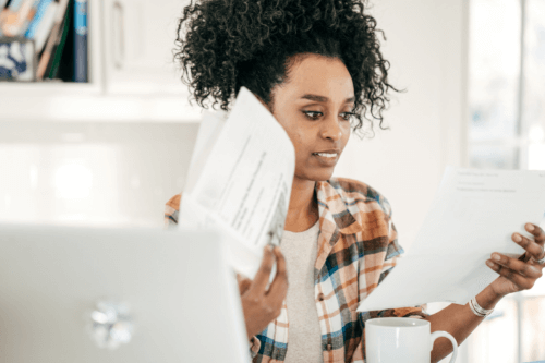 confused looking young african american woman looking at her taxes papers near laptop