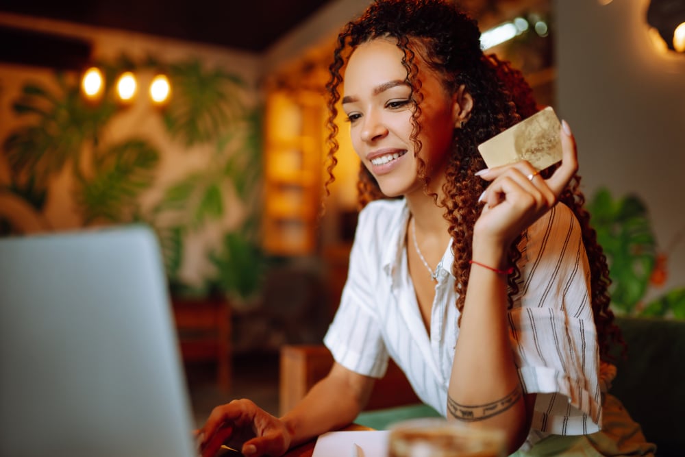 Festive Finances: Holiday Budget Tips | Sensible Services ABC. Young woman sitting in front of laptop holding credit card to make an online purchase.