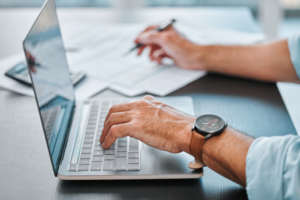 Professional Bookkeeping Services in Hammond, LA at Sensible Services ABC. Close-up of a person working on a laptop while reviewing documents and taking notes at a desk.